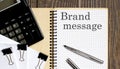 Notepad with text BRAND MESSAGE on the wooden background with clips, pen and calculator Royalty Free Stock Photo