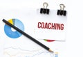 Notepad with text COACHING on business charts and pen