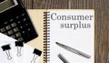 Notepad with text Consumer Surplus on wooden background with clips, pen and calculator Royalty Free Stock Photo