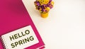 Notepad with text HELLO SPRING, pink folder with a bouquet of artificial flowers on a light table