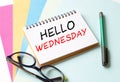 The Notepad with the text Hello Wednesday is on colored paper with glasses and a pen