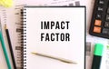 Notepad with text IMPACT FACTOR on the office desk, near office supplies. Business concept Royalty Free Stock Photo