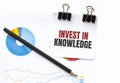 Notepad with text INVEST IN KNOWLEDGE on business charts and pen