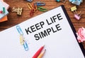 Notepad with the text KEEP LIFE SIMPLE on the table with colored paper clips and crumpled sheets