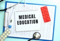 A notepad with the text MEDICAL EDUCATION lies on a medical clipboard with a stethoscope and pills on a blue background. Royalty Free Stock Photo