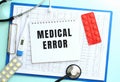 A notepad with the text MEDICAL ERROR lies on a medical clipboard with a stethoscope and pills on a blue background. Royalty Free Stock Photo