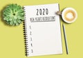 Notepad with text 2020 New Years Resolutions and numbered list on yellow desk with succulent plant and cup of coffee