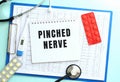 A notepad with the text PINCHED NERVE lies on a medical clipboard with a stethoscope and pills on a blue background. Royalty Free Stock Photo