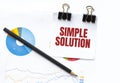 Notepad with text SIMPLE SOLUTION on business charts and pen