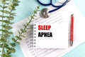 Notepad with text sleep apnea on top of diagnostic charts with stethoscope, red pen and eucalyptus Royalty Free Stock Photo