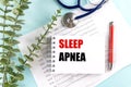 Notepad with text sleep apnea on top of sleep study charts with stethoscope, red pen and leaves on blue background Royalty Free Stock Photo