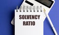 Notepad with text solvency ratio placed on top of calculator and pen on blue background Royalty Free Stock Photo