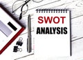 Notepad with text SWOT ANALYSIS, glasses, paper clips, white calculator and pen on desktop, top view Royalty Free Stock Photo