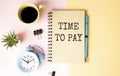 Notepad with text Time to Pay on the table with alarm clock, flower