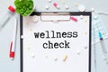 A notepad with the text WELLNESS CHECK lies on a medical clipboard with a stethoscope and pills on a blue background Royalty Free Stock Photo