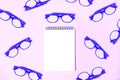 Notepad with trendy glasses on pastel pink violet background
