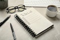 Notepad with unfilled To Do list, pens, glasses and cup of coffee light on grey marble table