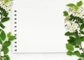 Notepad with white empty page and spring frame with twigs of small flowers and leaves on white background. Flat lay