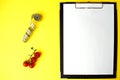 Notepad with a white sheet of paper for notes, next to it twisted centimeter and branch with red cherry tomatoes on a yellow Royalty Free Stock Photo