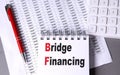 Notepad with the words bridge financing on financial spreadsheets with red pen and calculator Royalty Free Stock Photo