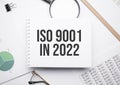 On the notepad for writing the text ISO 9001 in 2022, magnifier,charts and glasses