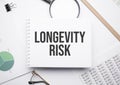 On the notepad for writing the text LONGEVITY RISK, magnifier,charts and glasses Royalty Free Stock Photo