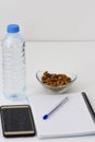 Notes, pen, smart phone, water botlle and the glass bowl filled with hazelnuts isolated on white background