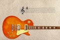Notes stave and honey sunburst vintage electric guitar at the bottom of rough cardboard background.