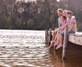 Nothing beats the annual family lake vacation. A happy family of four sitting on a jetty at the lake.