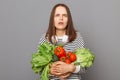 Nourishing food choices at the grocery store. Confused surprised woman embracing fresh vegetables returns from supermarket wearing