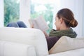 This novel is so engrossing. A relaxed young woman reading an engrossing novel on her couch.