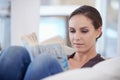 This novel is so engrossing. A relaxed young woman reading an engrossing novel on her couch.