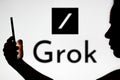 November 6, 2023, Brazil. A woman\'s silhouette holds a smartphone with the Grok logo in the backgroun