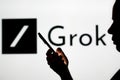 November 6, 2023, Brazil. A woman\'s silhouette holds a smartphone with the Grok logo in the backgroun