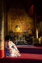 November 21th, 2018 - Ayutthaya & x28;THAILAND& x29; - Sitting woman in traditional dress looking at golden Buddha in thai temple Royalty Free Stock Photo