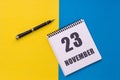 November 23th. Day 23 of month. Calendar date. Notebook with a spiral and pen lies on a yellow-blue background