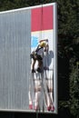 A worker hung on a rope changes an advertisement on a billboard