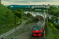 A passenger electric train moves along a river along the construction of urban buildings.