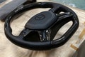 Carbon steering wheel of a black car in the workshop tightened and perforated with natural leather close up with the brand sign of