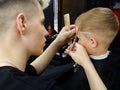 Caucasian hairdresser with scissors and comb cuts the boy in the Barber shop