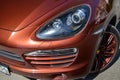 Front xenon headlight, drl and wheel view of Porsche Cayenne 958 2013 in brown color after cleaning before sale in a sunny summer