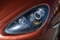 Front xenon headlight view of Porsche Cayenne 958 2013 in brown color after cleaning before sale in a sunny summer day with gray