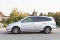 Left side view of a Honda Stream car in a silver body Japanese 2002 year van in a parking lot with a green trees and asphalt