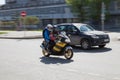 A pair of men in a red biker jacket and a woman in blue both in protective helmets on a black motorcycle with yellow body elements