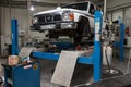 White used car Nissan Patrol raised on a blue lift for repairing the chassis and engine in a vehicle repair shop. Auto service