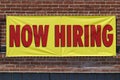 Now Hiring bright yellow banner sign with red print I