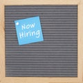 Now hiring message on sticky note on gray felt letter board