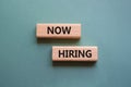 Now Hiring symbol. Concept word Now Hiring on wooden blocks. Beautiful grey green background. Business and Now Hiring concept.