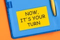 NOW ITS YOUR TURN the word is written in black letters on the yellow paper for notes Royalty Free Stock Photo