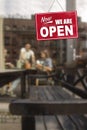 Now - We Are Open sign in front of blurred people outside a cafe enjoying diner, drinks and coffee. Royalty Free Stock Photo